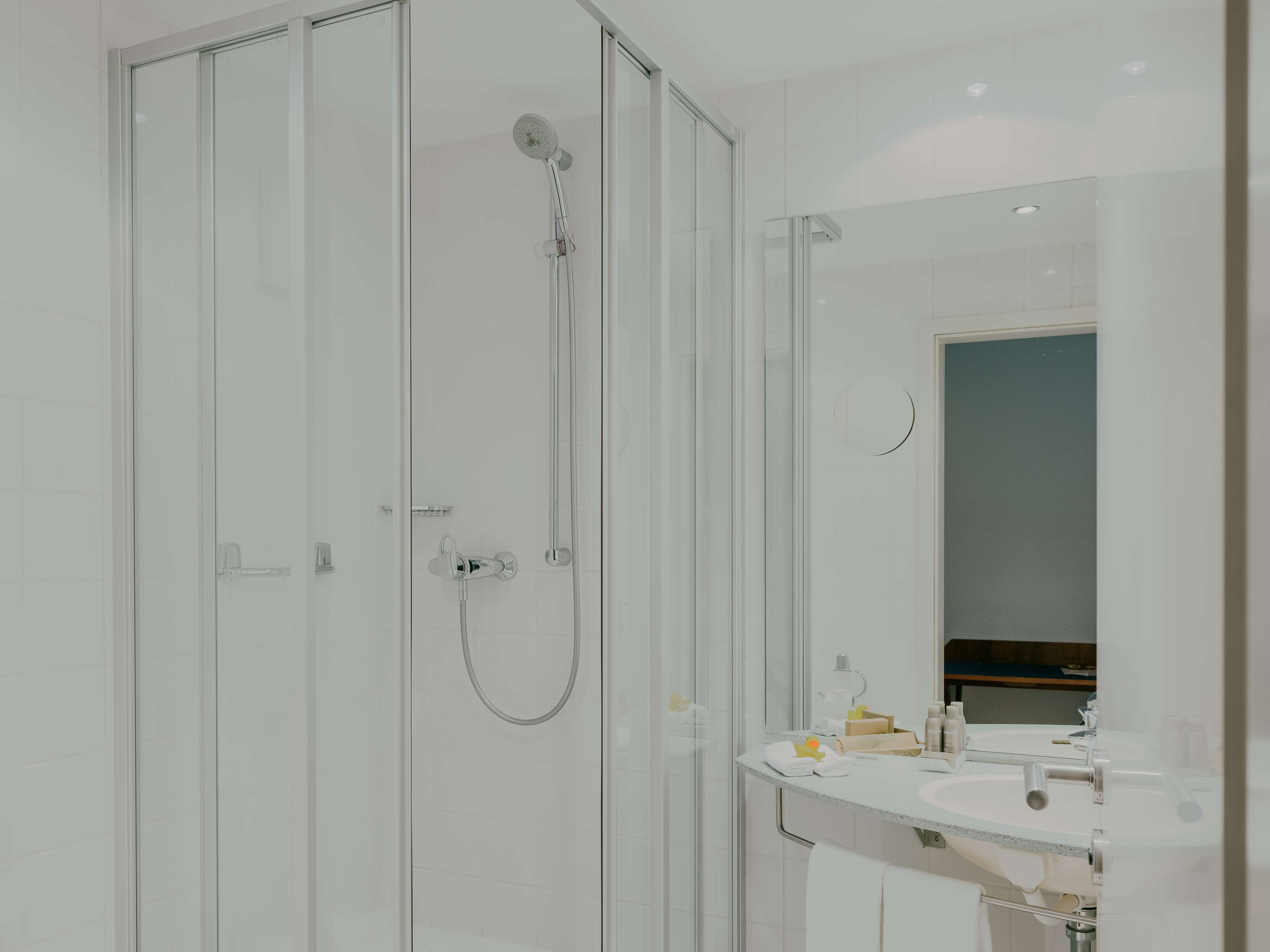 Un baño moderno con ducha de vidrio, lavamanos blanco y espejo.