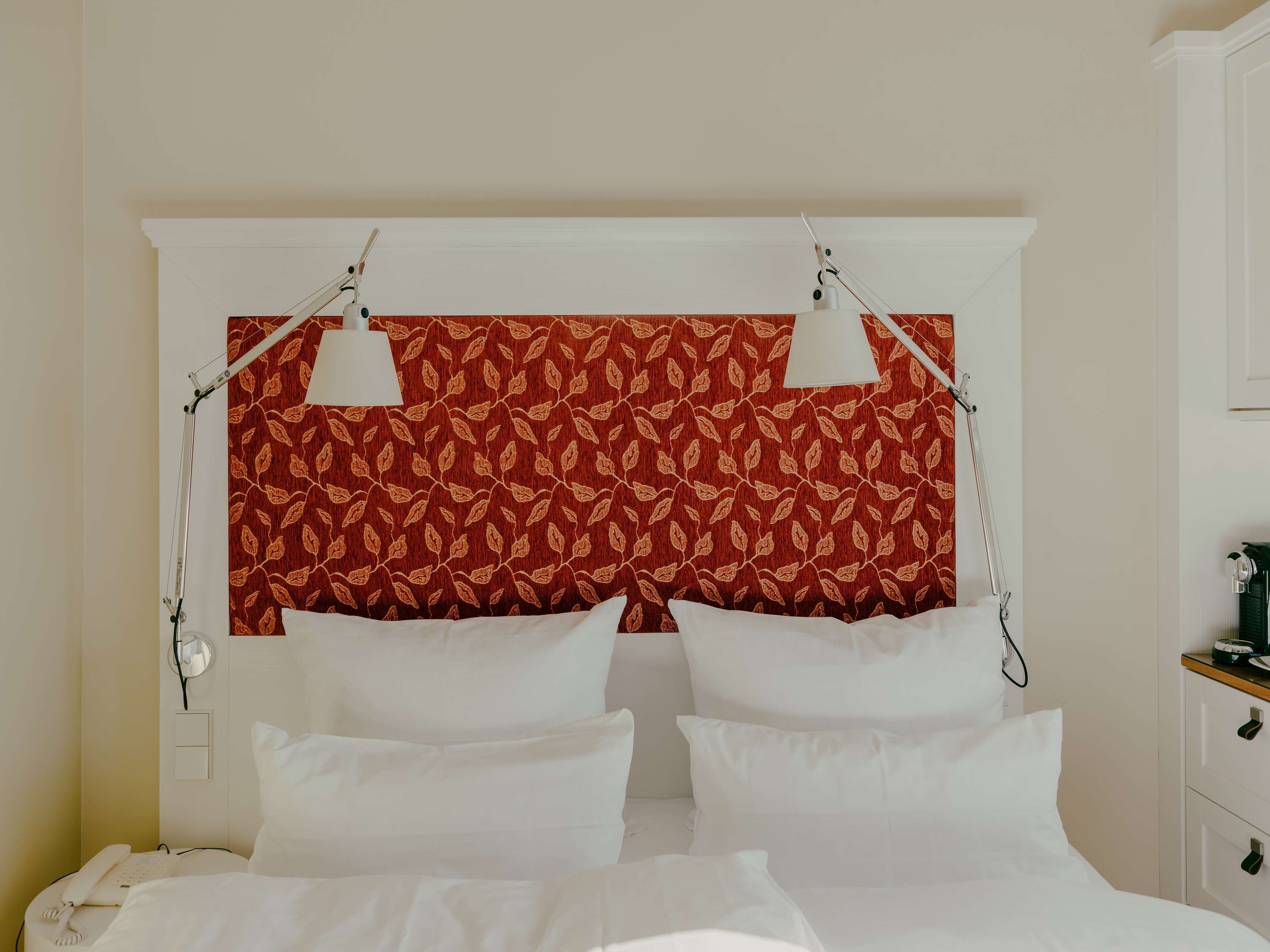 A hotel room with a bed, two bedside lamps, a telephone, and a patterned headboard.