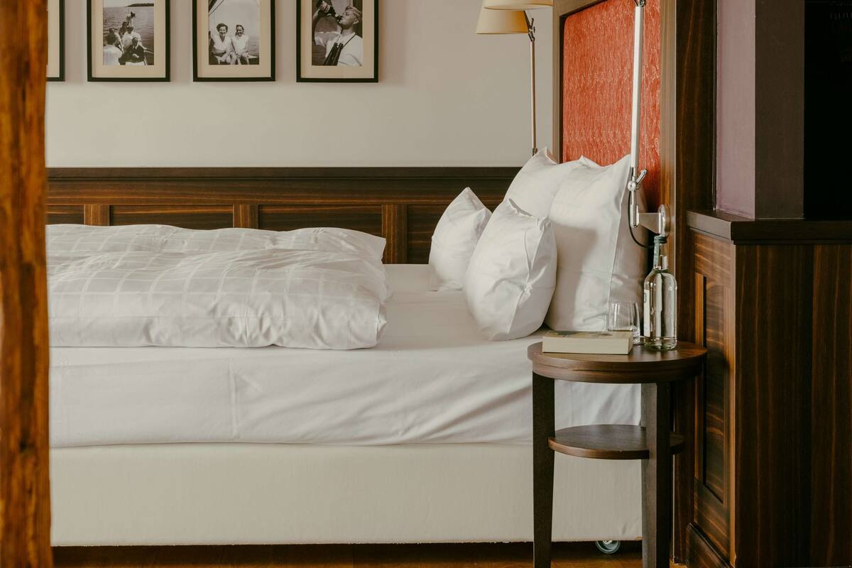 A neatly made bed with white linens, a bedside table with a lamp, and three framed photographs on the wall.