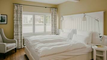 Ein Hotelzimmer mit einem großen Bett, einem Sessel, einem Nachttisch mit Lampe und einem Fenster mit Vorhängen.