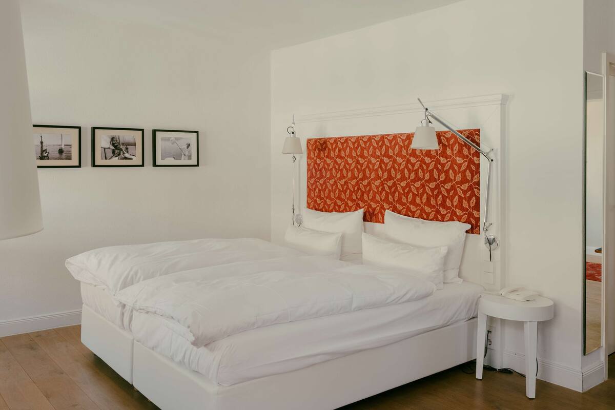 A white bed with a red patterned headboard, a bedside table with a lamp, and three framed pictures on the wall.