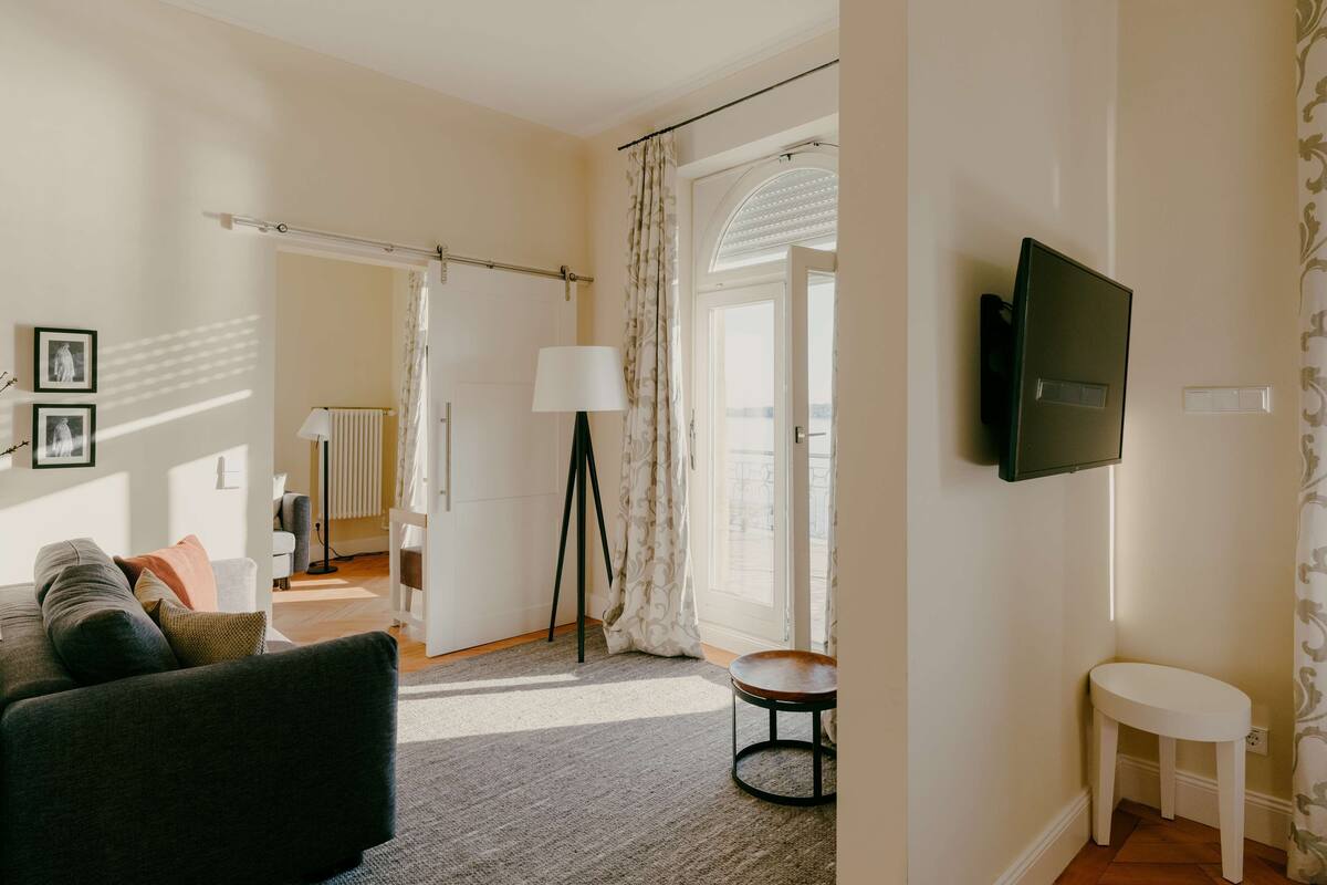A living room with a sofa, a small table, a lamp, and a TV mounted on the wall.