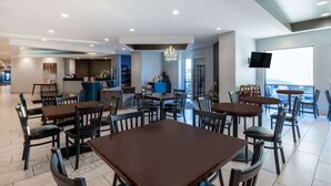 A modern dining area with multiple tables and chairs, a bar area, and a television mounted on the wall. - Baymont by Wyndham Rapid City (Rapid City)