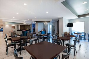 Un espace repas moderne doté de plusieurs tables et chaises, d’un bar et d’un téléviseur fixé au mur.