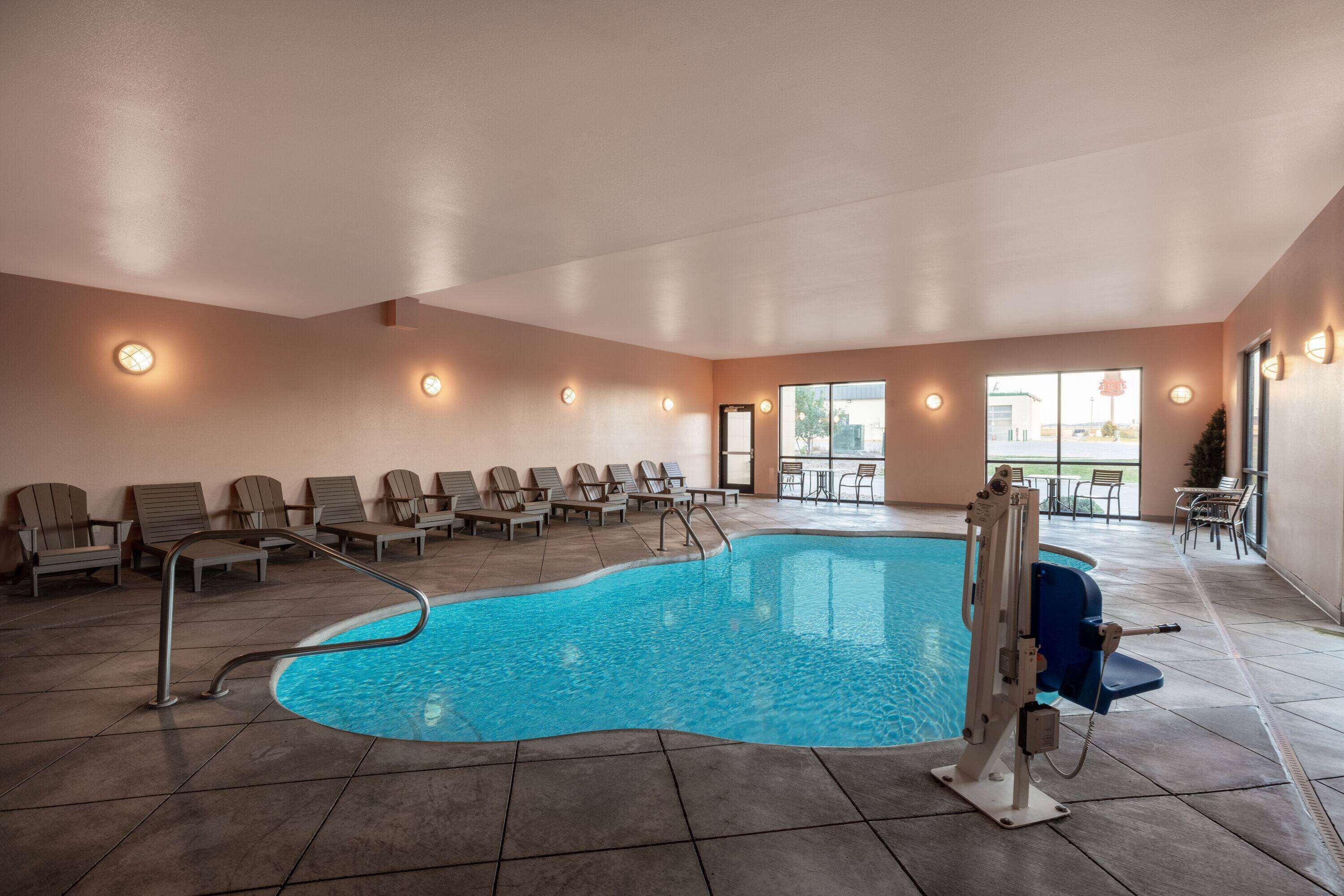 An indoor swimming pool with a clear blue water, surrounded by lounge chairs and a poolside table.