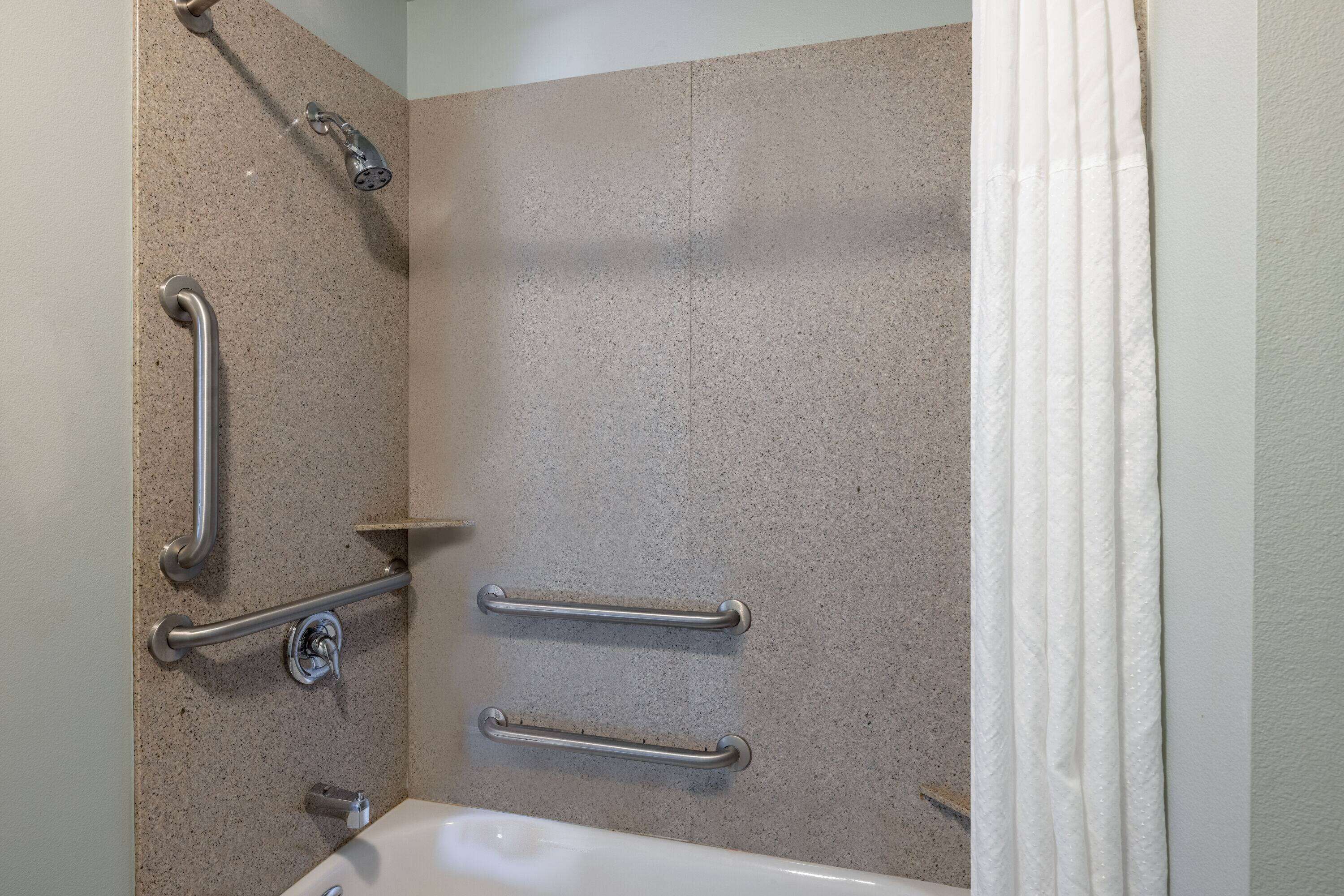 A bathroom with a bathtub, grab bars, and a shower head.