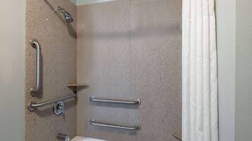 A bathroom with a bathtub, grab bars, and a shower head.