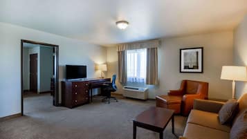 A hotel room with a desk, chair, television, and a sofa.