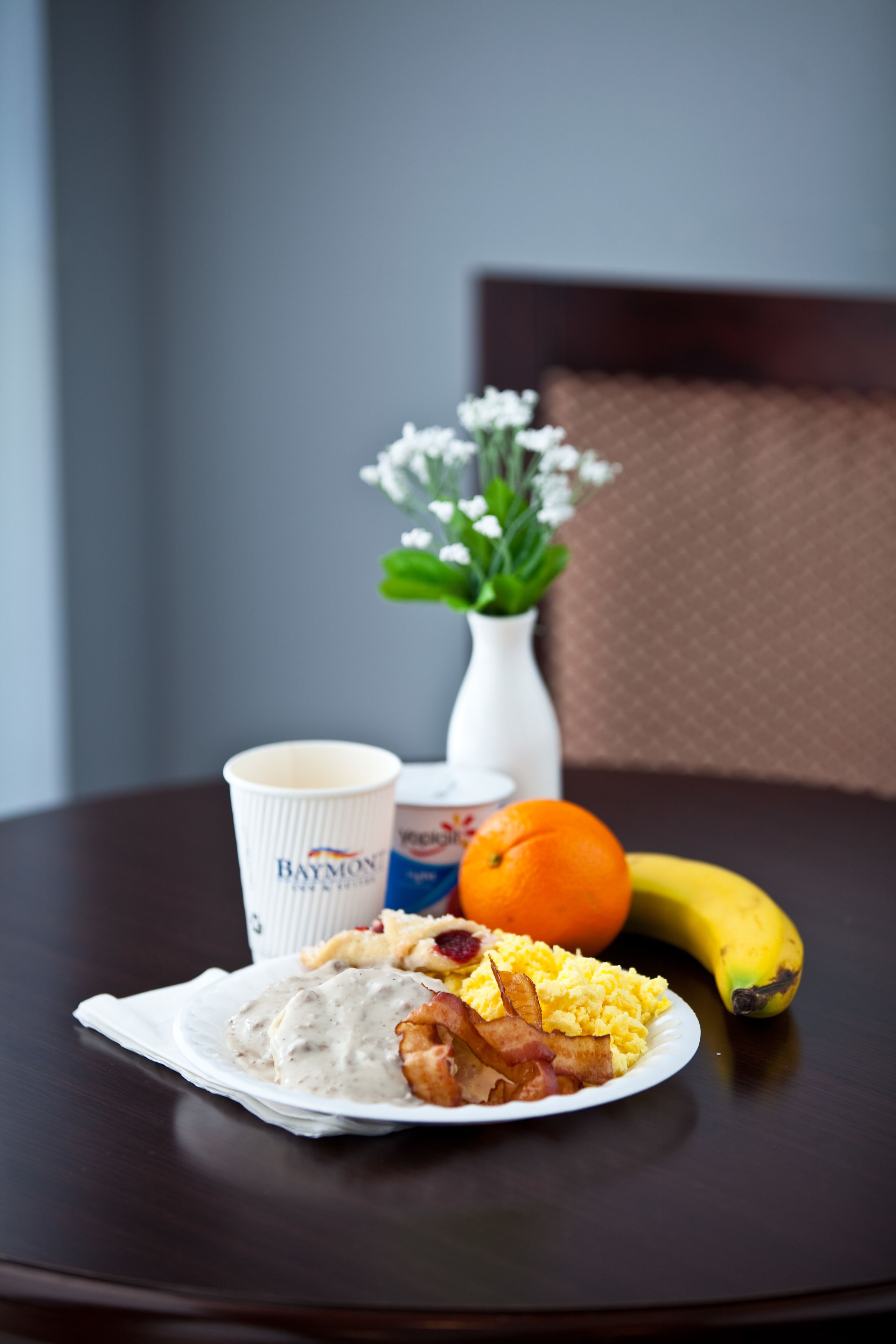 Un plato de desayuno con huevos, tocino y salsa, una banana, una naranja y una taza sobre una mesa.