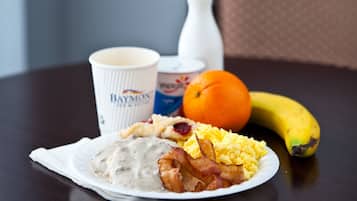 Un plato de desayuno con huevos, tocino y salsa, una banana, una naranja y una taza sobre una mesa.