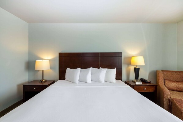 Una habitación de hotel con una cama grande, dos mesitas de noche, una lámpara, una silla y un cabecero.