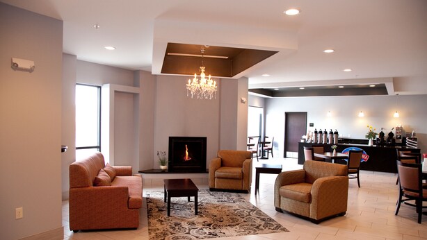 A spacious living room with a fireplace, a chandelier, and a dining area with a bar. - Baymont by Wyndham Rapid City (Rapid City)