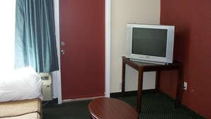 Ein Hotelzimmer mit einem Einzelbett, einem Fernseher auf einem Holzständer, einer roten Tür und einem blauen Vorhang.