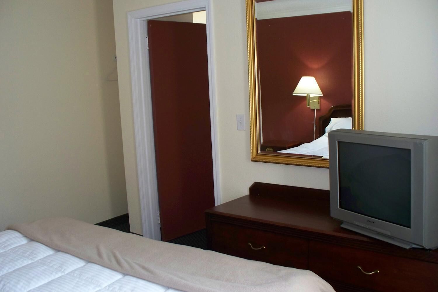 Une chambre d’hôtel avec un lit, une commode, une télévision et un miroir.