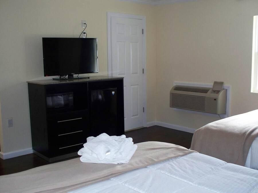 Habitación de hotel con cama, televisor en una cómoda, puerta blanca y equipo de aire acondicionado.