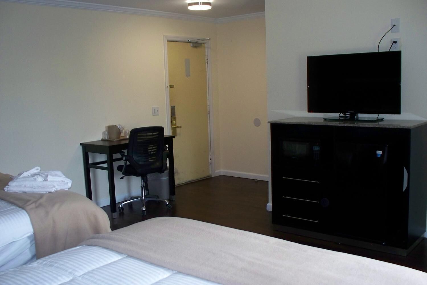 A hotel room with a bed, a desk with a chair, a television on a cabinet, and a door leading to another room.