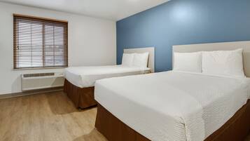 Habitación de hotel con dos camas, una ventana con persianas, un calentador de pared y una pared de acento azul.