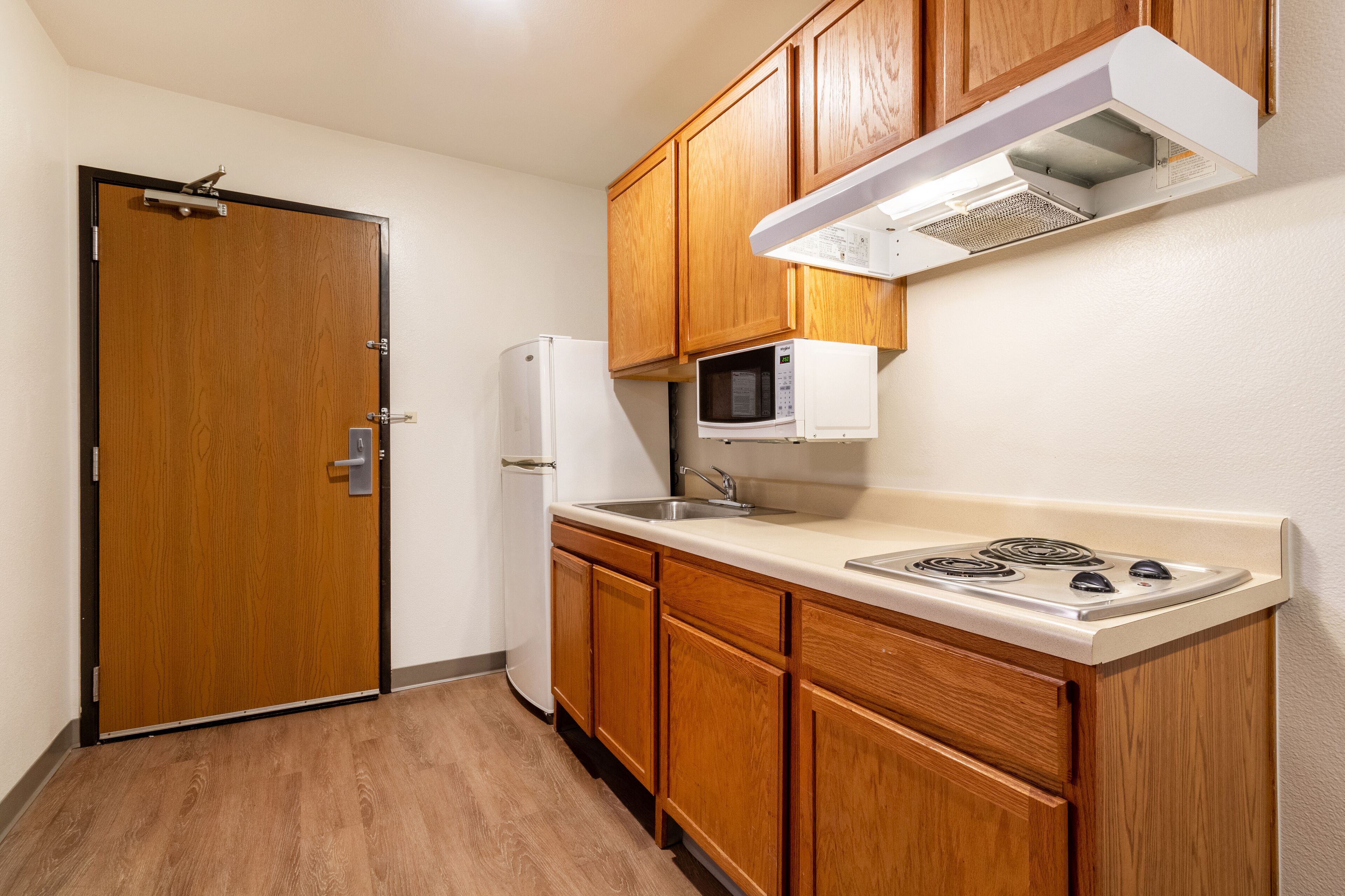 Una cocina compacta con armarios de madera, un microondas, un refrigerador y una estufa.