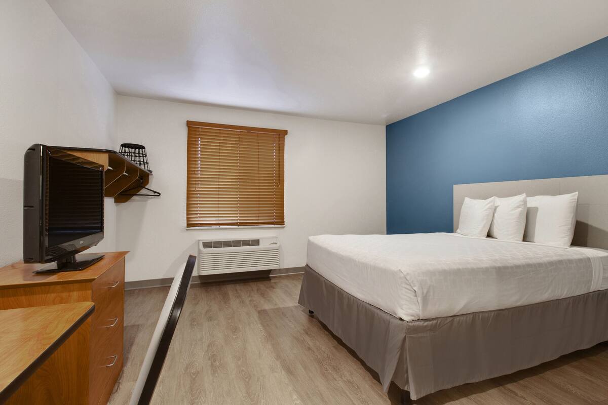 Un dormitorio con cama, escritorio con computadora, ventana con persianas y un calentador de pared.