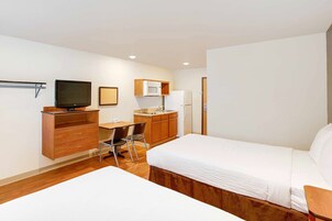 Habitación de hotel con cama, escritorio con silla, televisión, microondas y refrigerador.