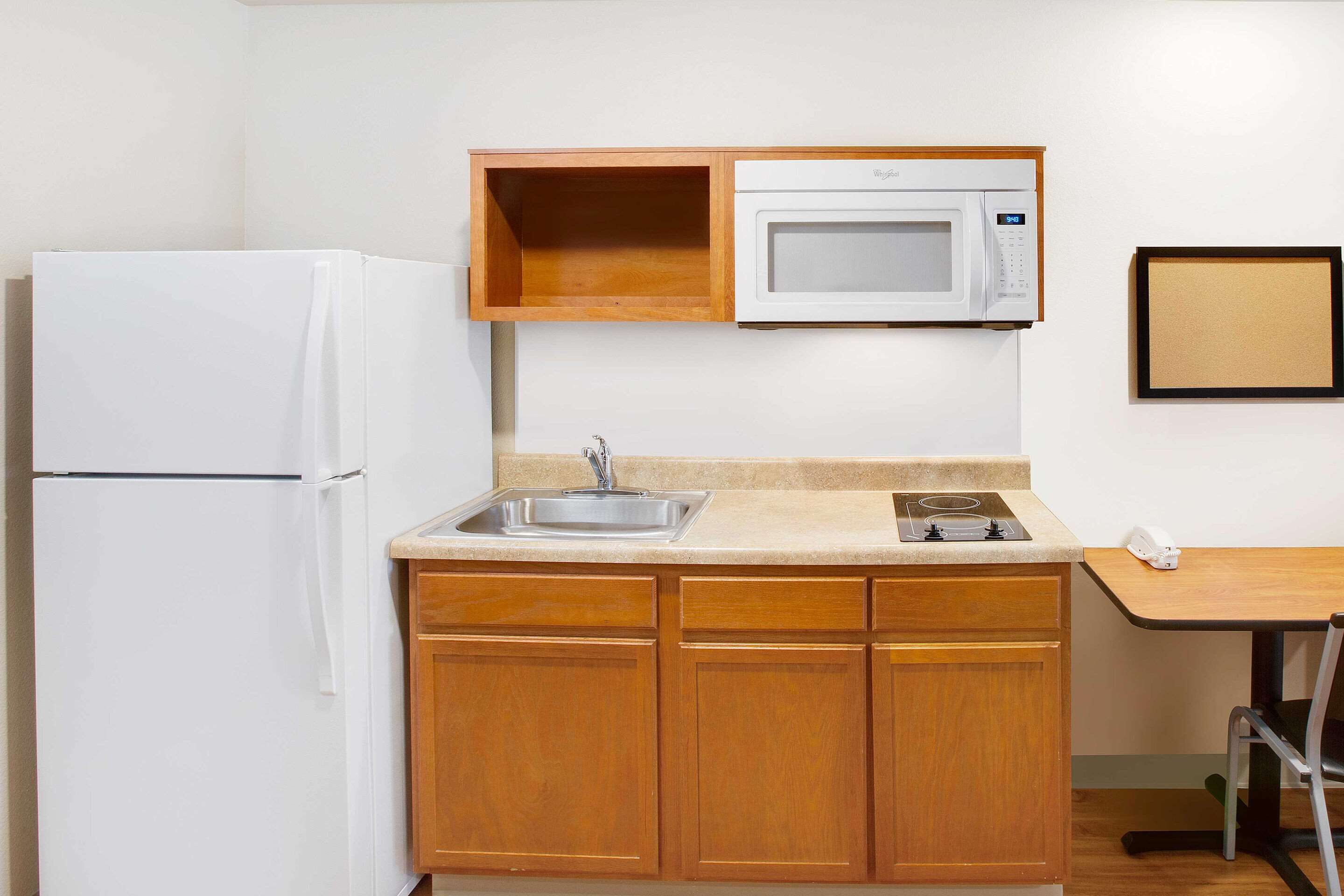Cocina compacta con refrigerador blanco, microondas, pileta y muebles de madera.