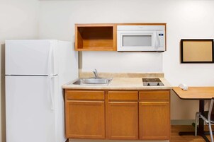 Cocina compacta con refrigerador blanco, microondas, pileta y muebles de madera.