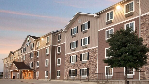A multi-story hotel with a stone facade, multiple windows, and a well-lit entrance. - WoodSpring Suites College Station (Bryan)