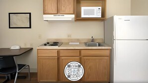 A compact kitchen with wooden cabinets, a microwave, a stove, and a refrigerator. - WoodSpring Suites College Station (Bryan)