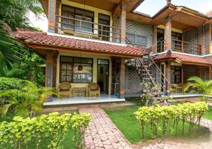 A two-story house with a balcony, a staircase, and a garden with plants and a pathway. - Lovina Beach Hotel (Buleleng)