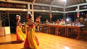 Una presentación de baile en un espacio al aire libre techado, con suelo de baldosas y mesas de madera preparadas para comer.