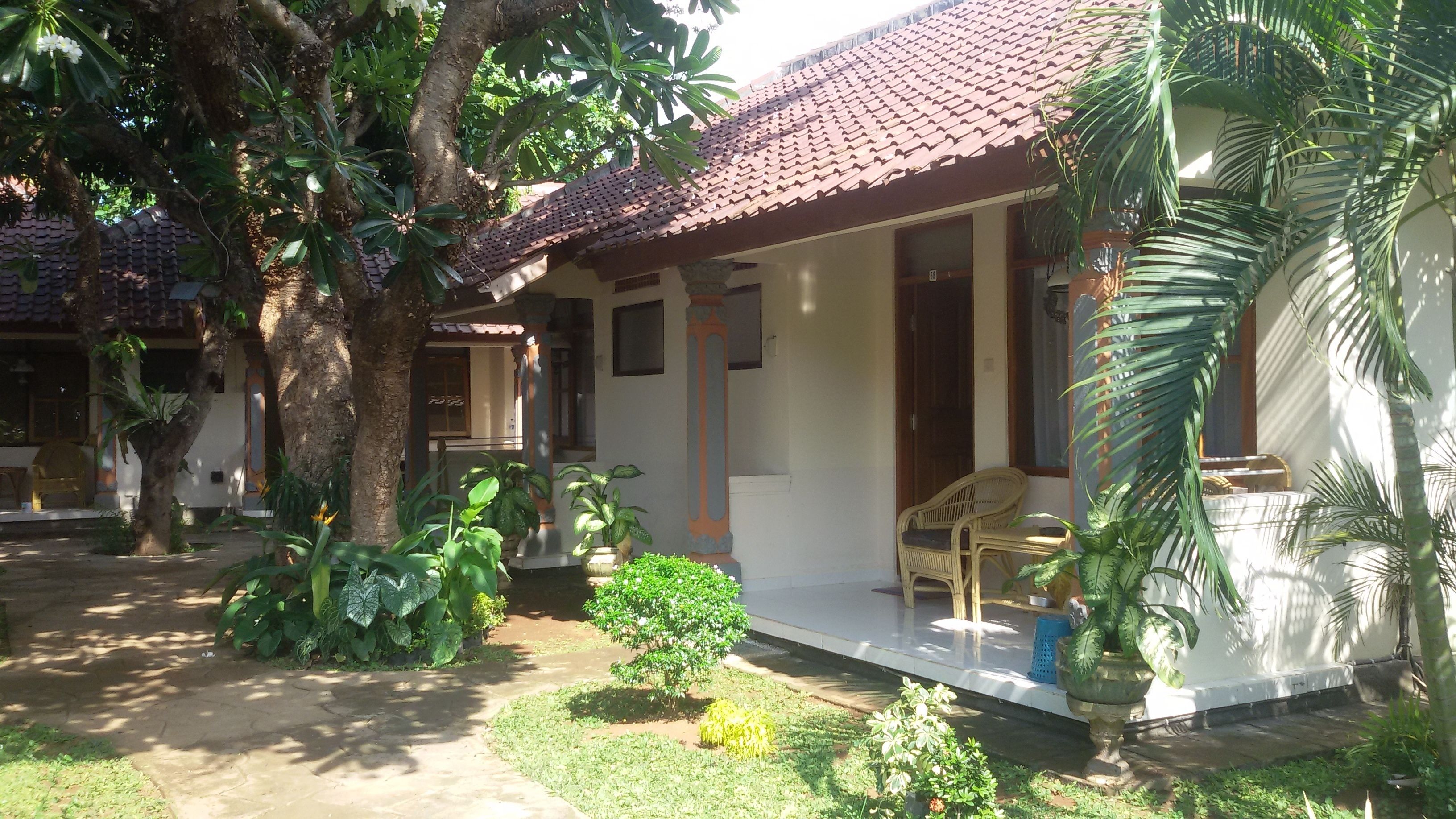 A house with a tiled roof, a porch with a chair, and various plants.