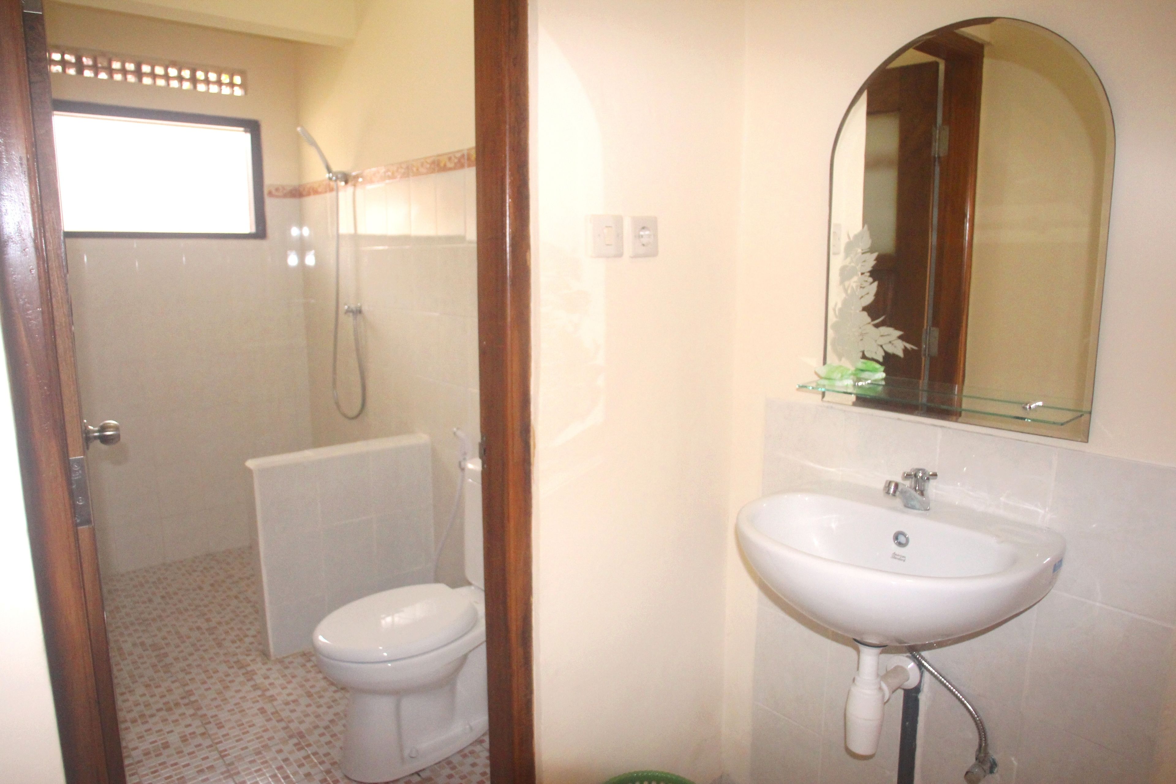 Un baño con inodoro, ducha, lavamanos y espejo con repisa de vidrio.