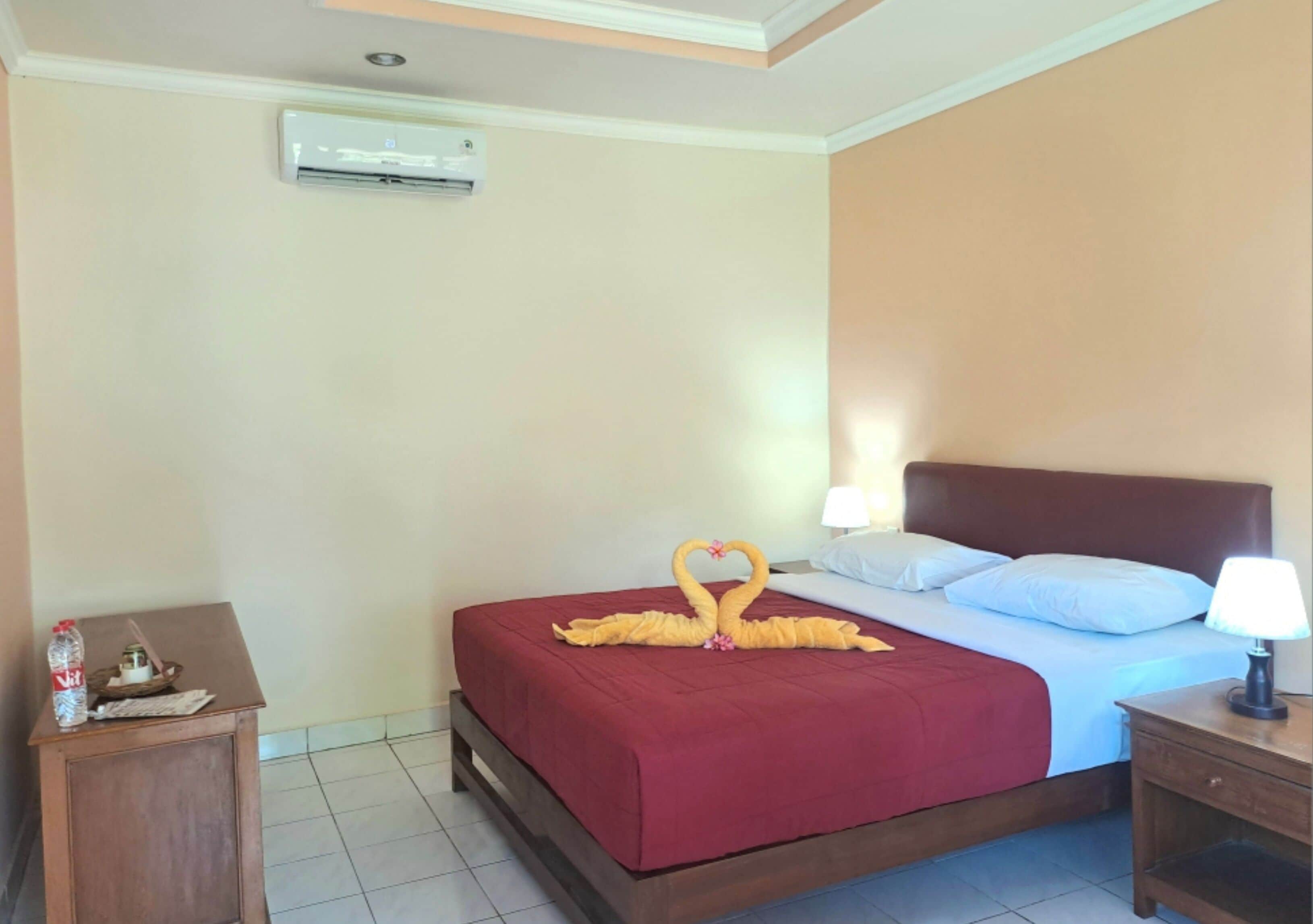 Habitación de hotel con cama, mesita de noche, lámpara y aire acondicionado instalado en la pared.