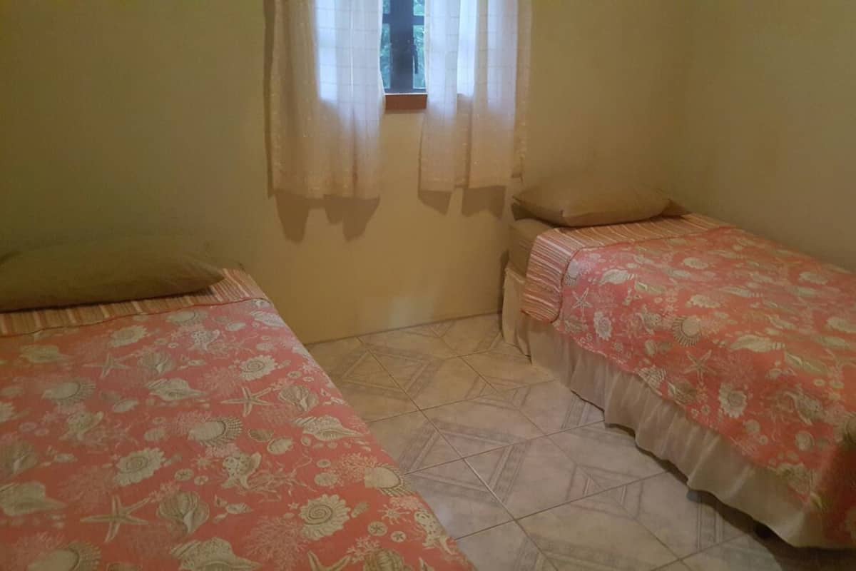 A small room with two single beds, a window with curtains, and a tiled floor.