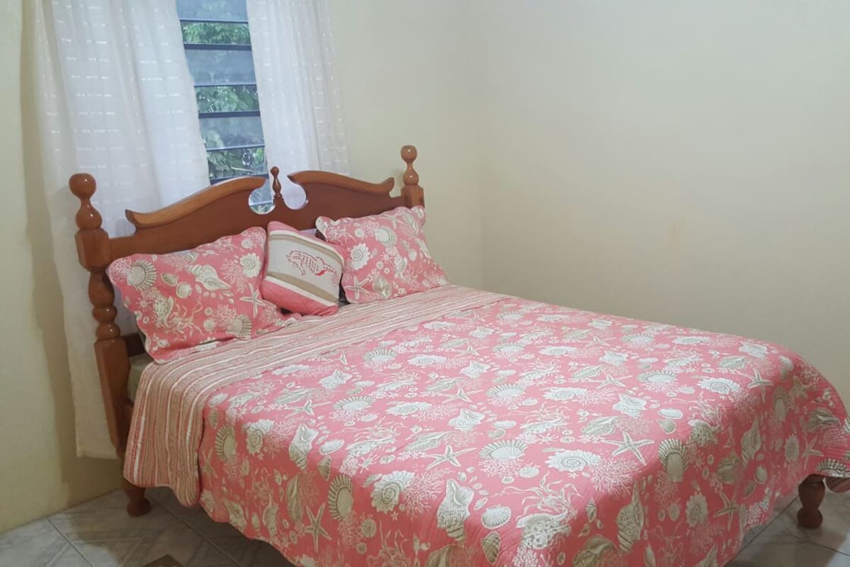 A bedroom with a wooden bed, pink floral bedding, and a window with sheer curtains.