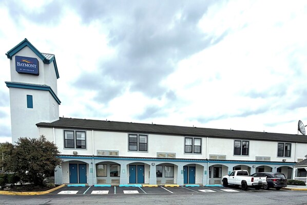 A Baymont motel with a prominent tower, multiple parking spaces, and a row of rooms with blue doors.