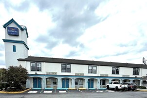 Un motel Baymont doté d’une tour imposante, de nombreux espaces de stationnement et d’une rangée de chambres avec des portes bleues.