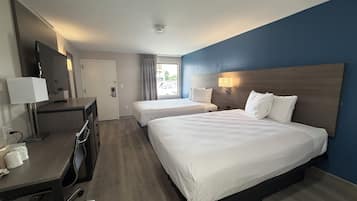 Habitación de hotel con dos camas, un escritorio con lámpara, televisión y ventana con cortinas.