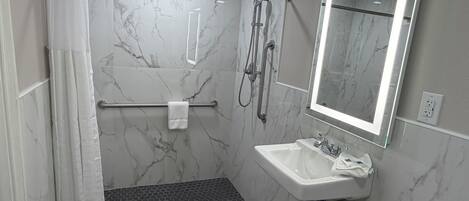 Une salle de bain moderne équipée d’une douche, d’un lavabo, d’un miroir et d’un porte-serviettes.