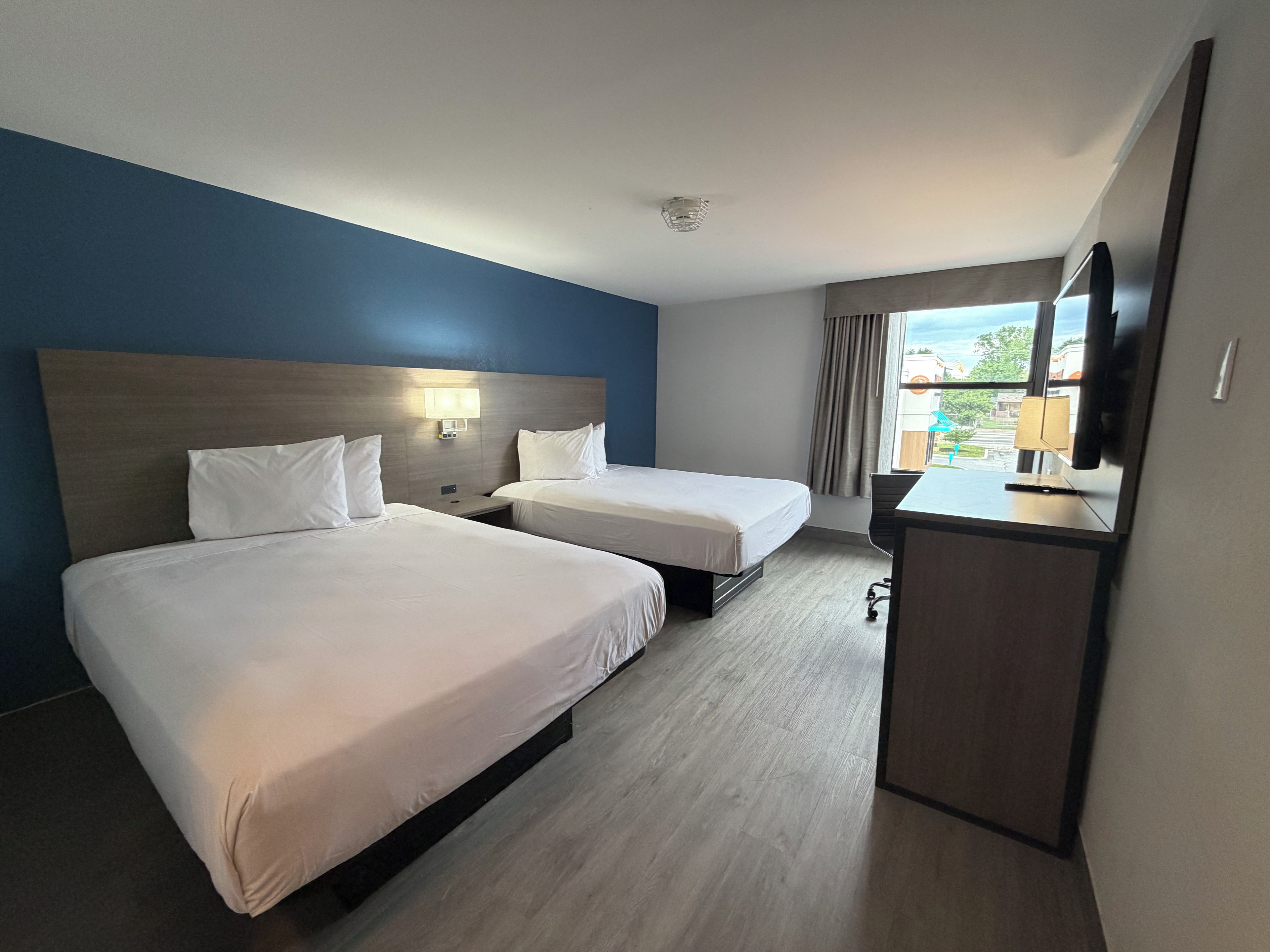 Habitación de hotel con dos camas, un escritorio, televisor y ventana con cortinas.