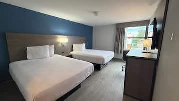Habitación de hotel con dos camas, un escritorio, televisor y ventana con cortinas.