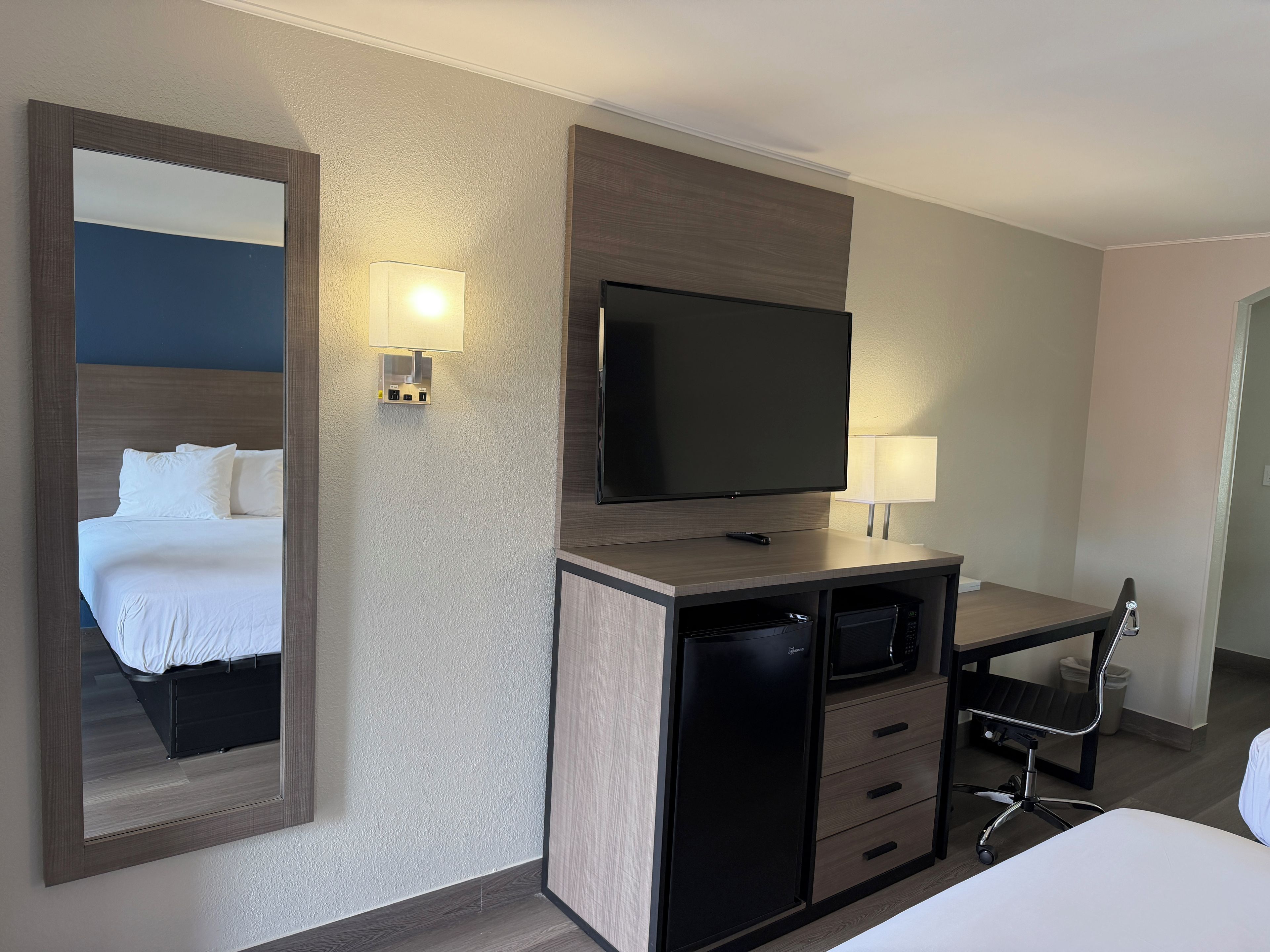 Een hotelkamer met een bed, een bureau met televisie, een stoel en een koelkast.