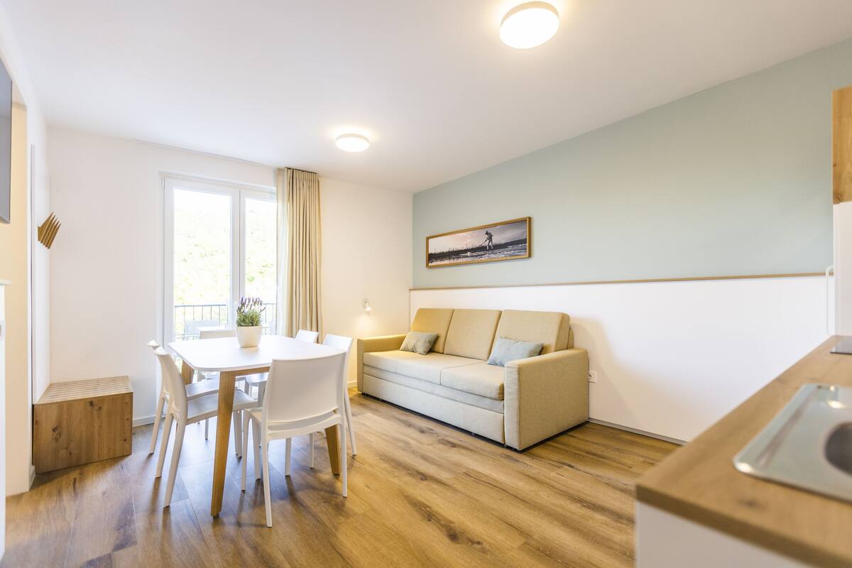 Una cocina moderna con piso de madera, una mesa de comedor con sillas, un sofá y un cuadro en la pared.