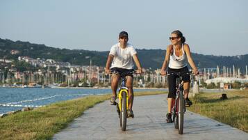 Two people riding bicycles on a concrete path by the water.