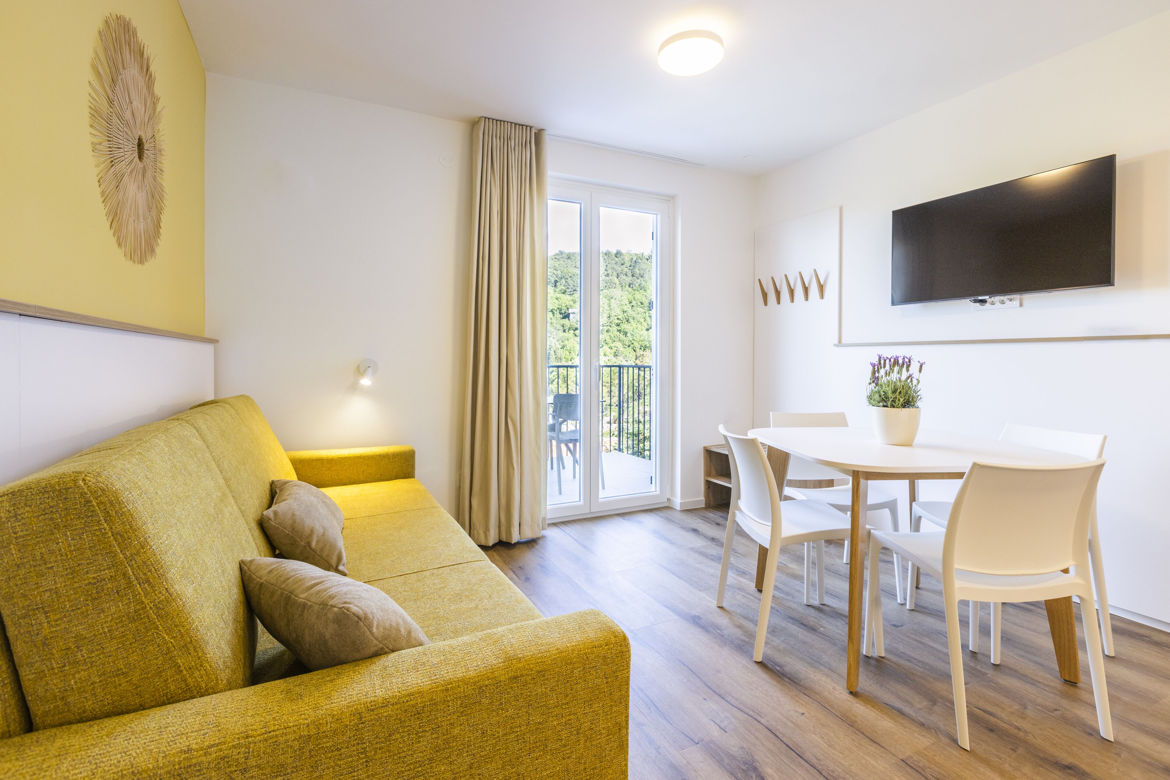 Un salon moderne comprenant un canapé, une table à manger avec des chaises, un téléviseur à écran plat fixé au mur et une porte-fenêtre coulissante donnant sur un espace extérieur.