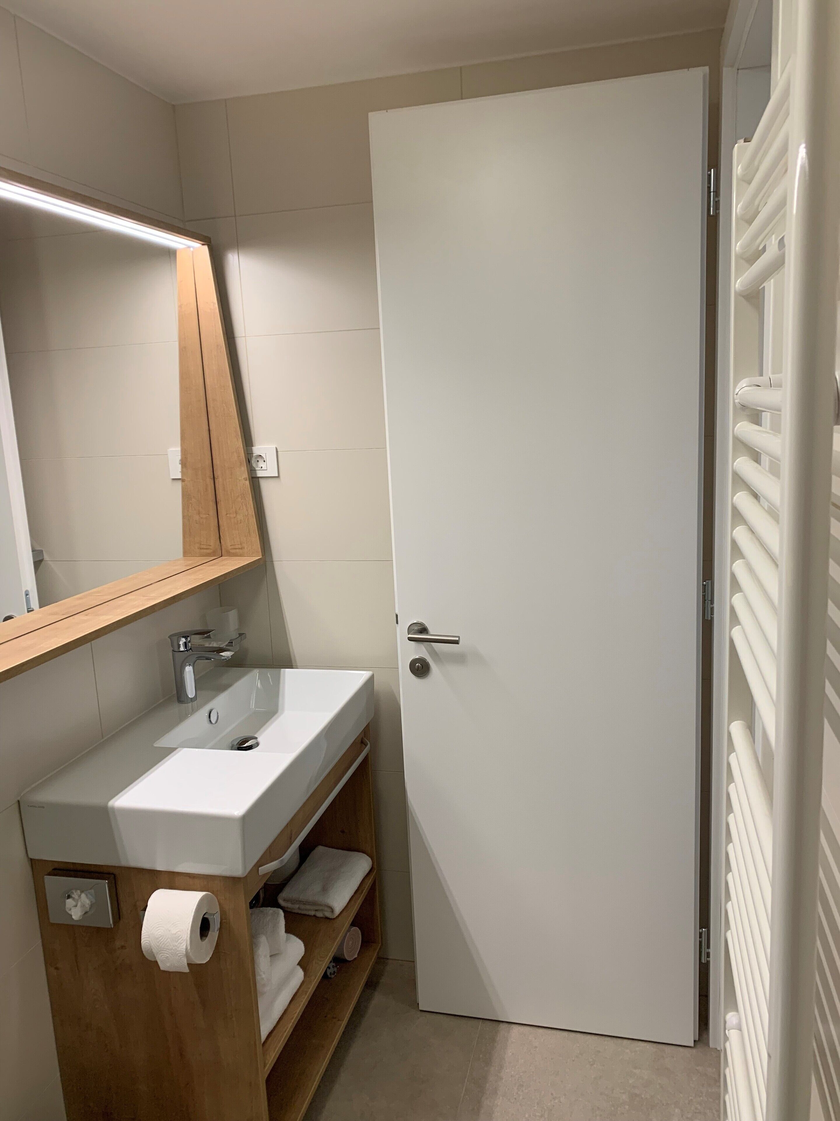 A bathroom with a white sink, wooden vanity, a mirror, and a white door.