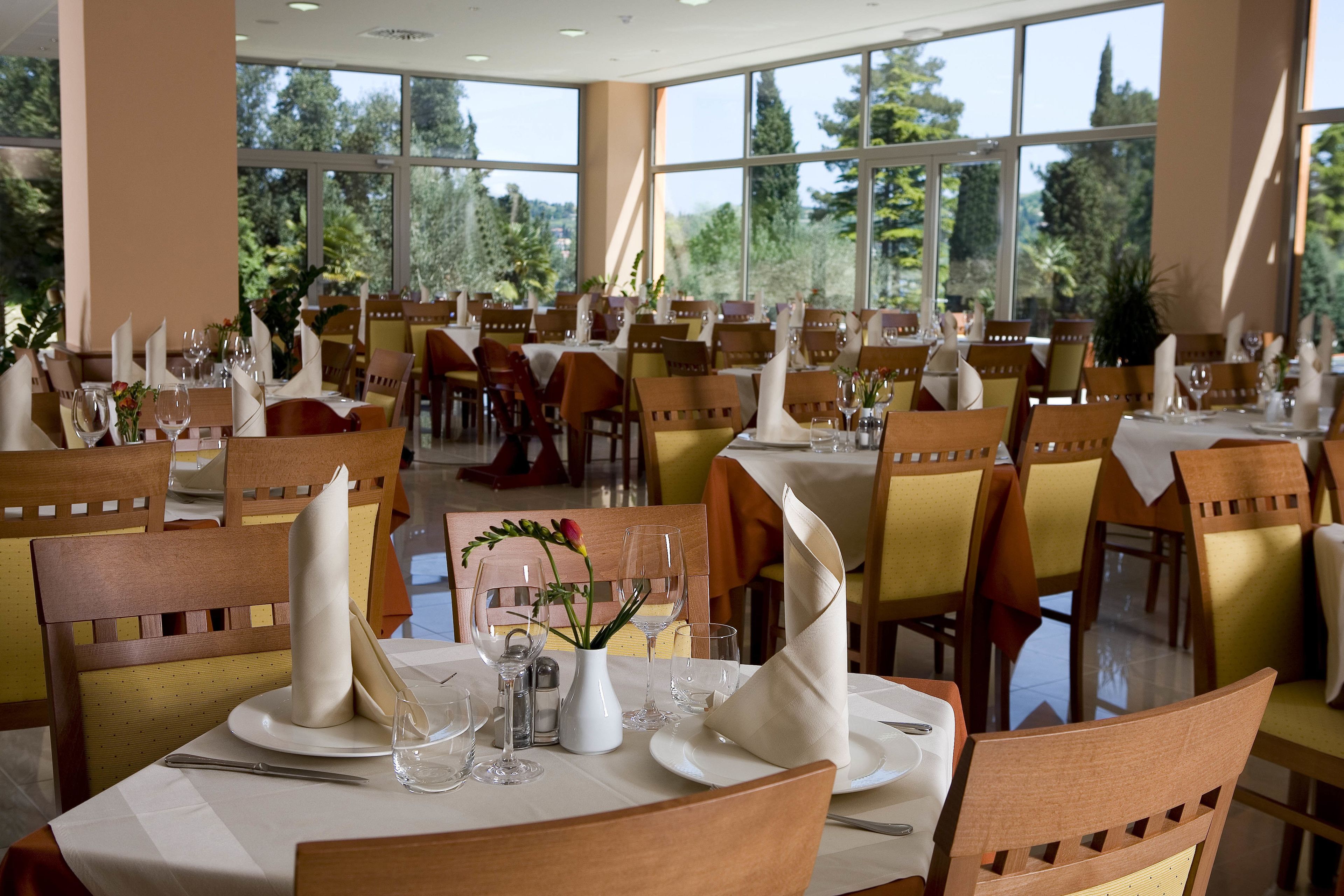 Un restaurante con varias mesas dispuestas para comer, con una vajilla ordenada y amplios ventanales que ofrecen vistas al exterior.