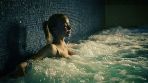 Una persona en un jacuzzi, con burbujas visibles y una pared de azulejos al fondo.