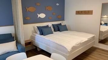 Un dormitorio con una cama grande, una mesita de noche, una silla, una pequeña mesa y una pared decorada con motivos de peces.