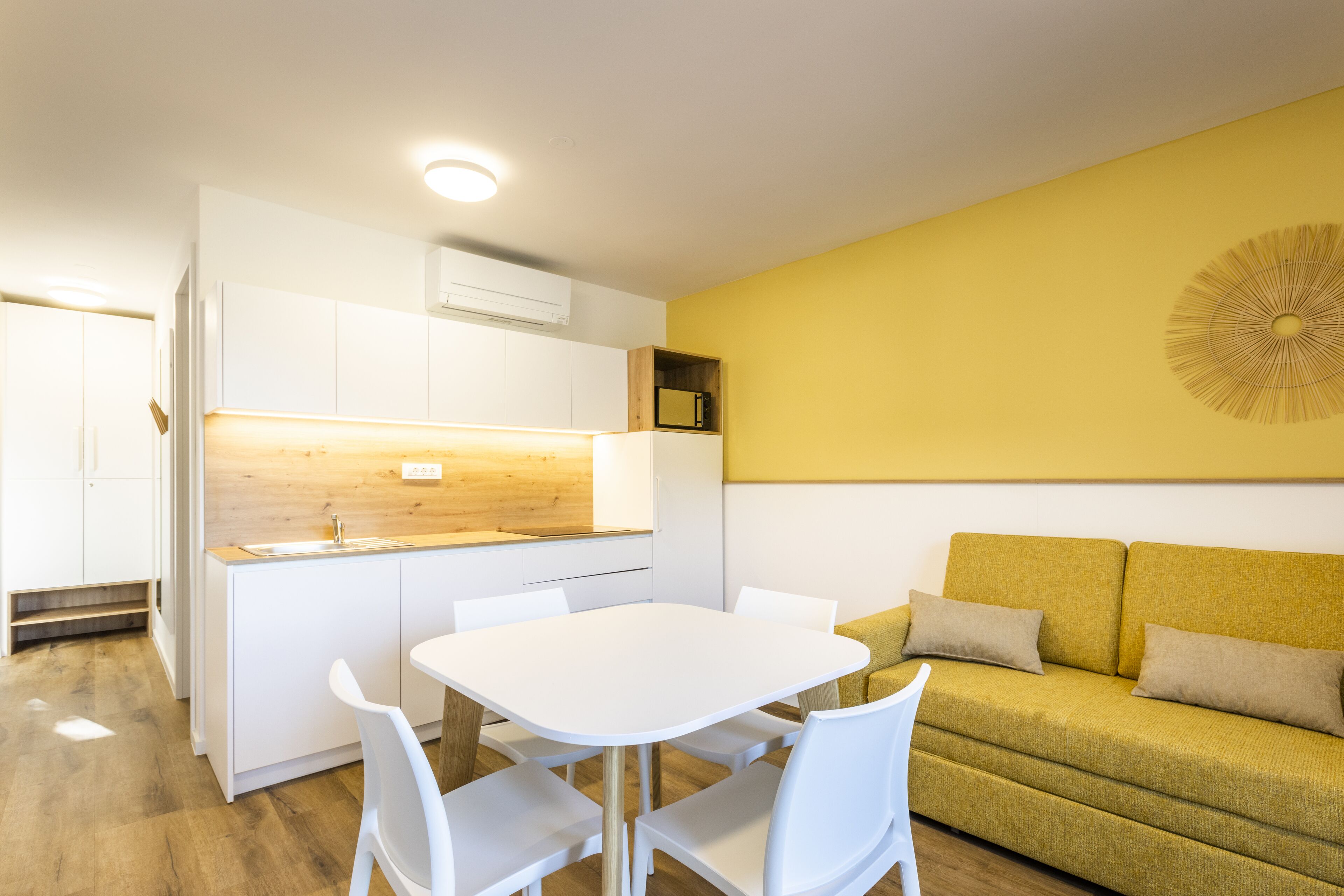 Une cuisine de taille réduite avec des meubles blancs, un plan de travail en bois et une table à manger avec des chaises.
